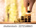 Small photo of Man hand hold the gold bar with high value for invest and stack picked up put on the old wood on the morning sunlight in public park, Targeting of business to winner and success concept.