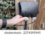 Small photo of Homeowner about to open the weatherproof cover of a double gang external electrical sockets. Seen in a garden after a heavy downpour.