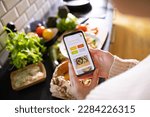 Young adult woman using a diet app on her phone while preparing a salad