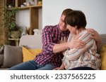 Small photo of Affectionate son, happy mother. young man wraps his arms around his elderly mother, in their cozy home setting. smiling mature woman, donning glasses, relishes authentic and loving connection