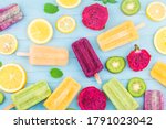 Various fruit popsicles are placed on the blue wooden board background, kiwi popsicles, orange popsicles, dragon fruit popsicles, cantaloupe popsicle