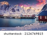 Impressive Winter landscape during sunset in Norway. Reine fjord image. Red fishing huts, fishboats and colorful sky over snowcapped mountains on background. Concept of an ideal resting place.
