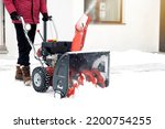 Closeup of red snow blower in action. Senior mature man outdoor in front of house using snowblower machine for removing snow on yard. Snow thrower in winter outside home. Young worker guy blowing snow