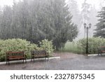 Small photo of Rain with hail on a summer day. Large puddles on the sidewalk during heavy rain. Heavy rain in the park. Wet benches on a paved path. Spray drops and bubbles in large puddles.