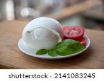 White ball of Italian soft cheese Mozzarella di Bufala Campana served with fresh green basil and red tomato