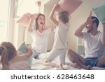 Family having funny pillow fight on bed. Parents spending free time with their daughters. 