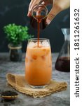 Small photo of A hand pouring black aroma tea into a glass of traditional Thai iced tea with milk latte.It is a mix of spices, sugar, sweetened condensed & evaporated milk sold on many streets of Thailand