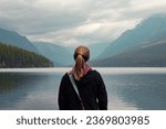 Woman standing looking at blue lake and mountains
