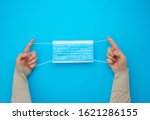 Small photo of female hands protracted blue sterile textile medical mask with white elastic bands for doctors on a light blue background, flat lay
