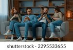 Small photo of Group friends business people sit on couch with mobile phones chatting in social media ignoring each other multiethnic addicted women and men use diverse devices modern tech addiction gadgets overuse