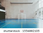 Small photo of Front view of the court in the gymnasium hall; an indoor modern office stadium with a basketball basket and hoop, football goal, blue floor, a concrete wall with an undeployed projection screen above