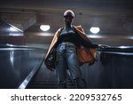 A stylish young black female in a coat and with a clutch is descending using an escalator; a fashionable very short-haired African woman on the moving staircase of the metro or an underground passage