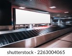 Shot in low-key of a very large rectangular blank billboard mockup facing a baggage claim in an airport terminal; a big white blank advertisement template indoors in front of a baggage handling system