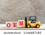 Small photo of Toy forklift hold letter block M in word OEM (abbreviation of original equipment manufacturer) on wood background