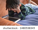 Small photo of Little asian boy lying on sofa alone playing tablet computer ipad, he bend down head in his hands, feeling upset, stressful, tired. Digital Addiction, Brain Impairment, Screen time, Self-absorption.