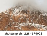 Small photo of A mountain in Zion National park, Utah, USA is laced with snow that highlights the rugged fins in the Navaho Sandstone, and partly shrouded by clouds that hide the tip of the peak.
