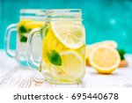 Lemon water, lemonade in mugs with handles, mason jar on a white wooden table. Cut Lemons in the background. Natural lemonade.