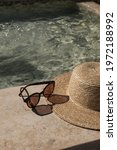 Small photo of Sunglasses and straw hat on marble swimming pool side with clear blue water with waves sunlight shadow reflections. Minimal fashion aesthetic summer vacation creative background