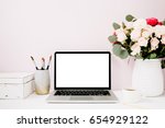 Home office desk with blank screen laptop, beautiful roses and eucalyptus bouquet, white vintage casket in front of pale pastel pink background. Blog, website or social media concept .
