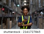 Small photo of Young smart African American woman working in warehouse using the tablet for stock checking and inspection the boxes, logistic warehouse to deliver the shipment, happiness worker with smiling face