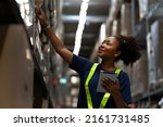 Small photo of African American worker checking the stock on shelf in warehouse comparing the balancing number in system after delivery shipment. Using tablet to update online stock available for selling on website