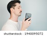 Small photo of Young man watches his phone and secretly takes photo. Portrait of mustachioed man illegally taking photo on phone camera. Pervert, violation of private space concept.