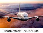 Passenger plane in the sunset sky. Aircraft flying above the clouds. Airplane front view.