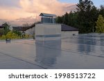 Flat roof covered with bitumen membrane and silver lacquer with chimney on a private house. Reflections after rain