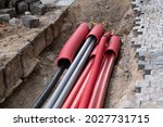 A large number of electric and high-speed Internet Network cables in red corrugated pipe are buried underground on the street covered with cobblestones. 