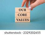 Small photo of Our core values symbol. Wooden blocks with words Our core values. Business man hand. Beautiful blue background. Business and Our core values concept. Copy space.