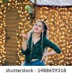 Small photo of Inordinate young woman with dreadlocks hairstyle and fashionable summer clothes throws an apple against the background of garlands