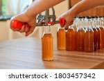Small photo of Using hand capper for home brewing. Background of brown bottles with homemade liquor or alcohol. Selective focus.
