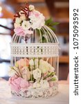 Small photo of Wedding romantic decor for guests dinner tables or gifts and guestbook tables, with white vintage decorative birdcage filled with white and pastel colored roses and spring flowers