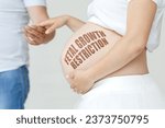 Small photo of A pregnant woman holds her husband's hand on her stomach with the inscription - Fetal growth restriction, a question mark. Pregnancy concept.