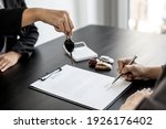 Small photo of The renter is signing a car rental agreement with the car rental company. After discussing the details and charges with the employee, the employee hand over the car keys to the renter.