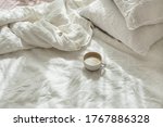 Cup of fresh coffee in bed, morning mood. Linen cotton textile bedclothes. Organic and natural linen. Cozy bedroom interior. Beautiful light.