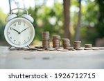 Small photo of Alarm clock and a pile of golden coins on the table, Concept of opportunity cost time and Money saving. Arrange coins into heaps with hands, content about money.