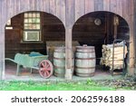 Small photo of Traditional farm setting with a wheel barrow, casks and billets of wood in a wooden barn