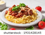 Pasta spaghetti bolognese with minced beef sauce, tomatoes, parmesan cheese and fresh basil in a plate on white table. Italian food