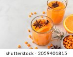 Small photo of Sea buckthorn autumn tea with orange in glass cups with fresh berries, cinnamon and rosemary on white table. Herbal vitamin tea. Hot autumn drink
