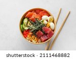 Tuna poke bowl salad in paper box or package for take away or food delivery with chopsticks on white background. Top view. Healthy food