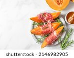 Melon cantaloupe slices with prosciutto ham, rosemary and honey in a plate on white background. Italian appetizer. top view. Healthy food