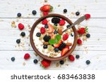 bowl of oat granola with yogurt, fresh raspberries, blueberries, strawberries, blackberries and nuts with spoon on white wooden board for healthy breakfast, top view