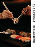 Small photo of Man and woman pick up sushi with chopsticks at the same time