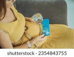 Prenatal Vitamins. Portrait Of Beautiful Smiling Pregnant Woman Holding Pill Box and a glass of water, Taking Supplements For Healthy Pregnancy While Sitting On Couch At Home, Free Space