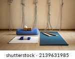 Small photo of Empty fly yoga Iyengar class with inventory for physical training. Yogi props rope on wall, wooden plank, bolster weighting agent with sand, brick and strap. Professional supply for therapy workout