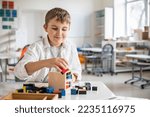 Happy male kid assembling Montessori material trinomial cube at school classroom desk. Smiling child boy learning mathematic algebra geometry alternative educational method construction wooden block