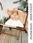 Small photo of A little girl in a salty blooper sits on a chair near the palm trees. The concept of relaxation and fun. Carefree childhood. Helping children with special needs.