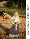 Small photo of A young woman walking through a field in the summer in the village met a prodigal horse and decided to pet him.