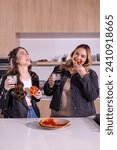 Small photo of A vertical shot capturing the joy of a plus-size woman taking a bite of pizza, while a mid-size woman laughs heartily with a pizza in hand.